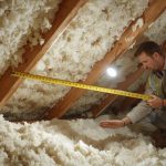 Homeowner inspecting attic insulation depth with a ruler against joists, showing clearly visible measurement markings