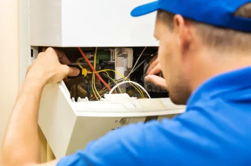 Engineer in a blue cap and blue shirt using a screwdriver on the wiring inside an open wall mounted boiler