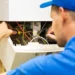 Engineer in a blue cap and blue shirt using a screwdriver on the wiring inside an open wall mounted boiler